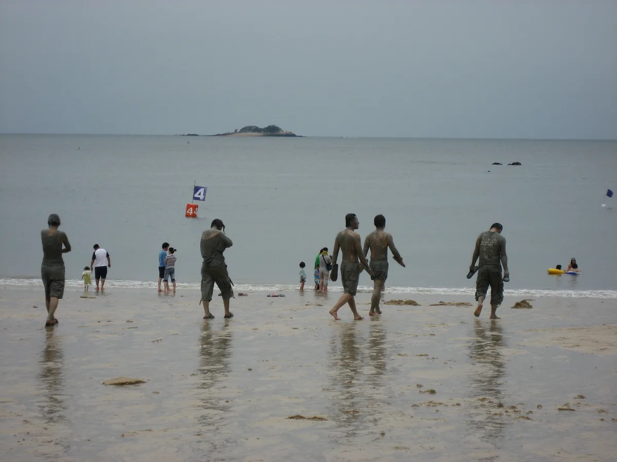 Visitors covered in mud walking along the shoreline at Daecheon Beach during the Boryeong Mud Festival