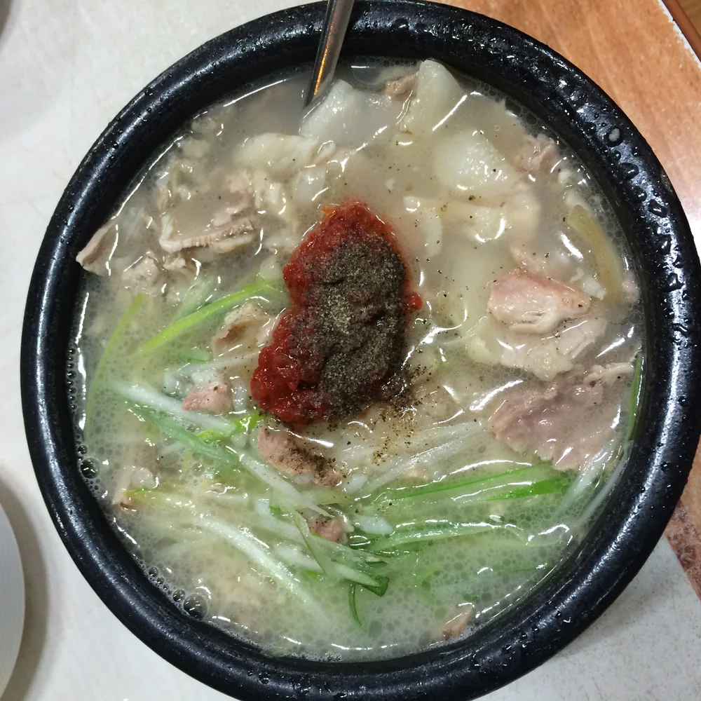A bowl of dwaeji-gukbap, Busan's pork and rice soup, topped with green onion and served with chili paste