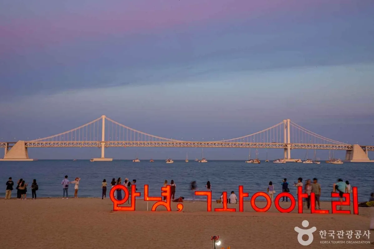 Gwangalli Beach at dusk with the illuminated Gwangan Bridge in the background and a lit sign reading Hello Gwangalli in Korean