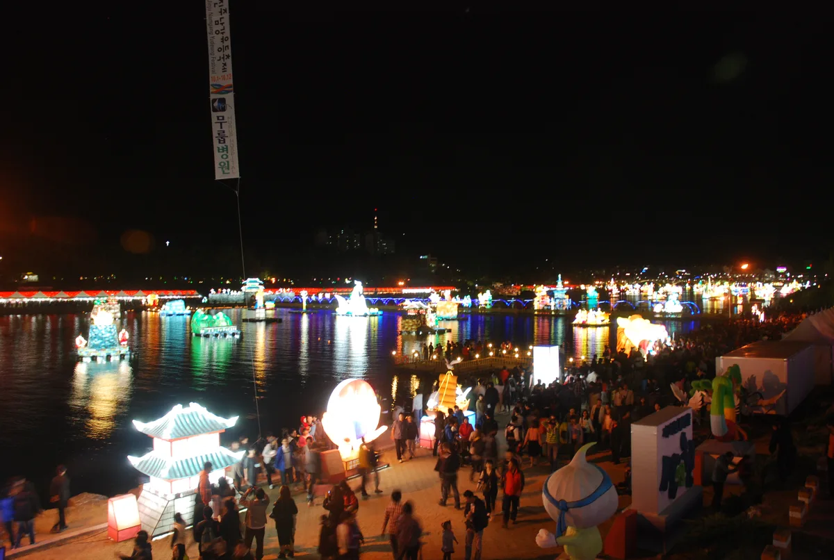 Illuminated floating lanterns shaped like traditional structures and figures on the Namgang River at night during the Jinju Namgang Yudeung Festival