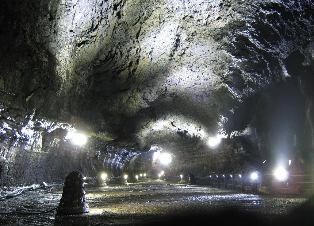The illuminated interior of Manjanggul lava tube cave on Jeju Island, showing the rough volcanic rock ceiling and walkway
