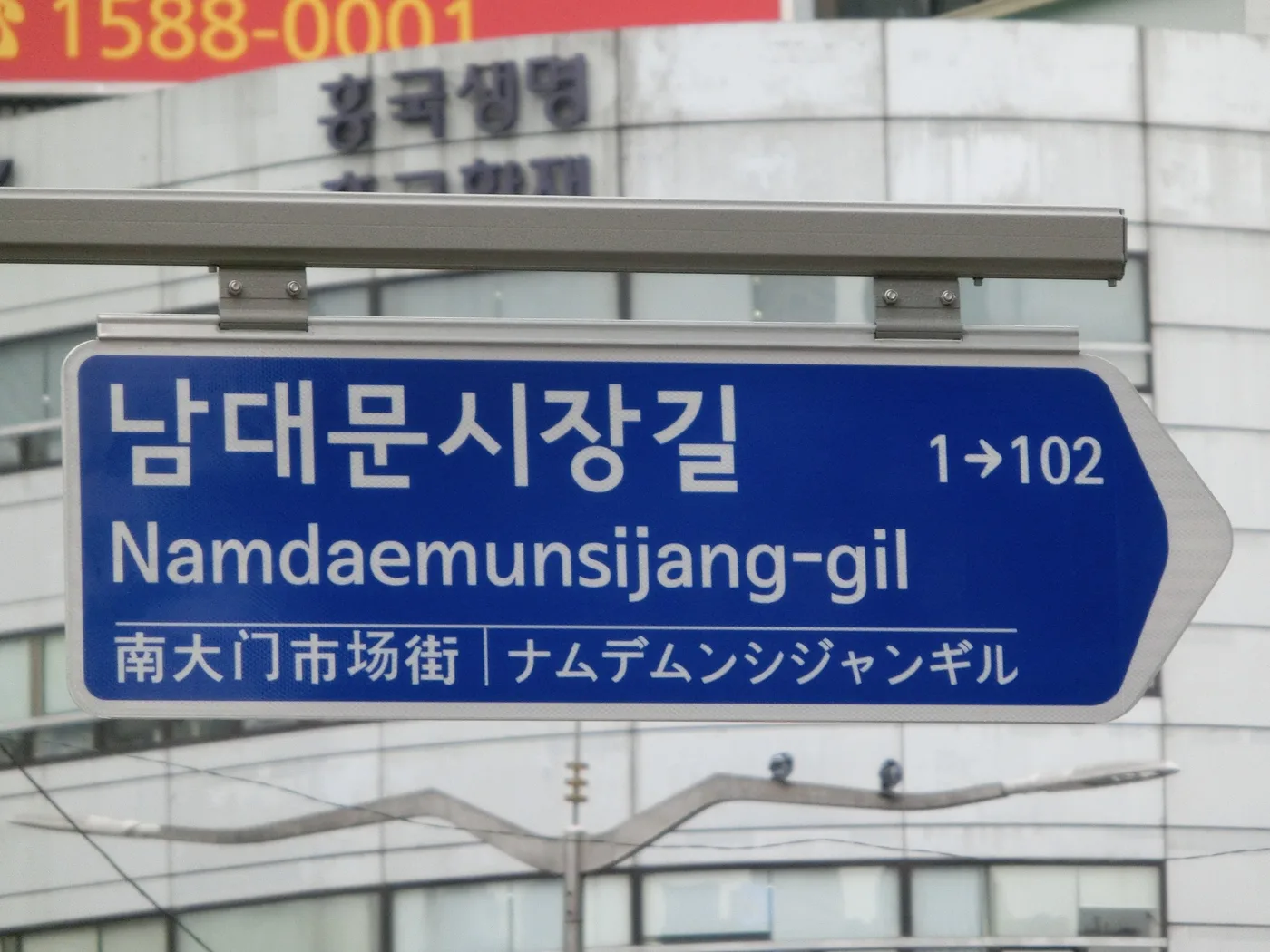 Blue Korean street sign for Namdaemunsijang-gil showing Hangul, English romanization, Chinese, and Japanese