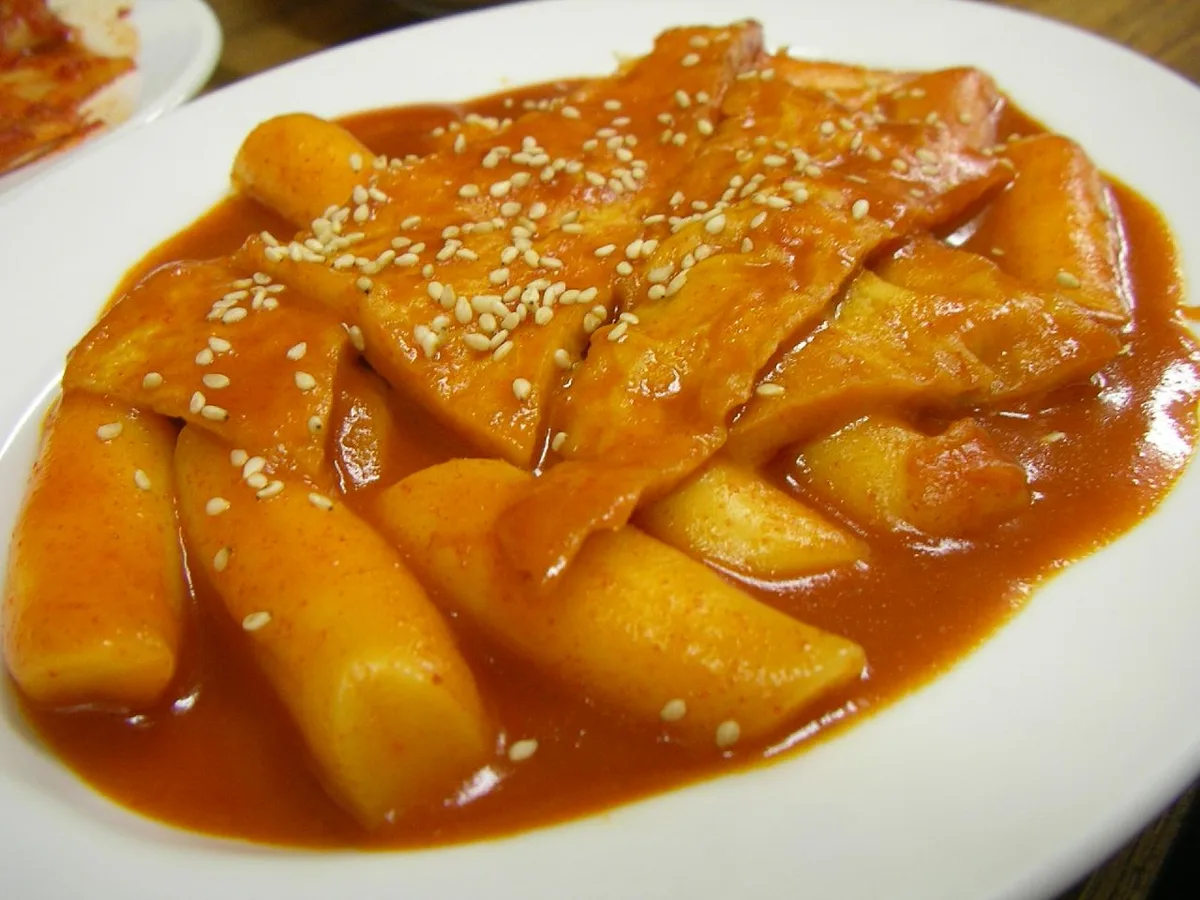 Close-up of tteokbokki, chewy Korean rice cakes covered in a glossy spicy red sauce and sprinkled with sesame seeds